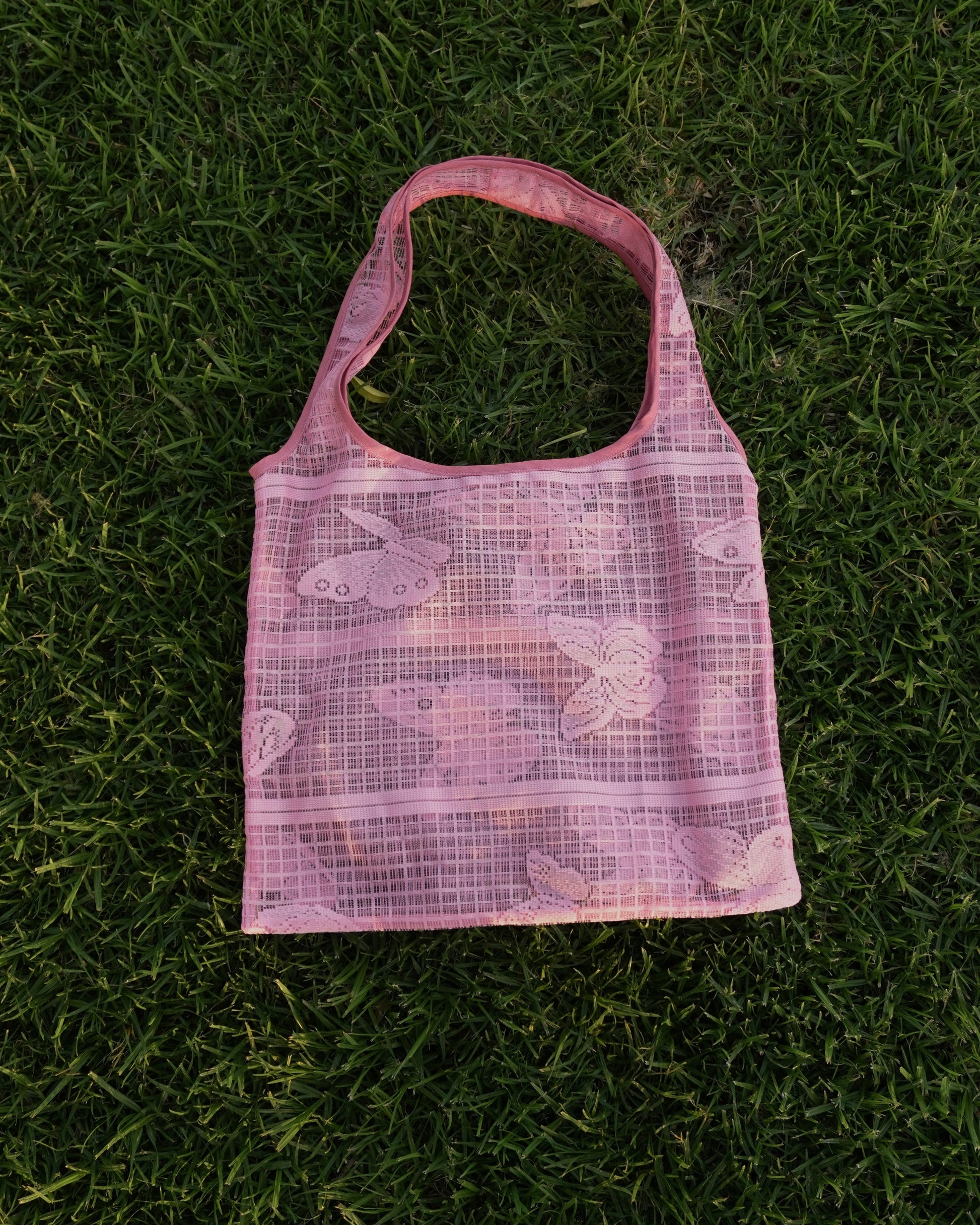 Pink mesh bag with floral patterns on a grassy background